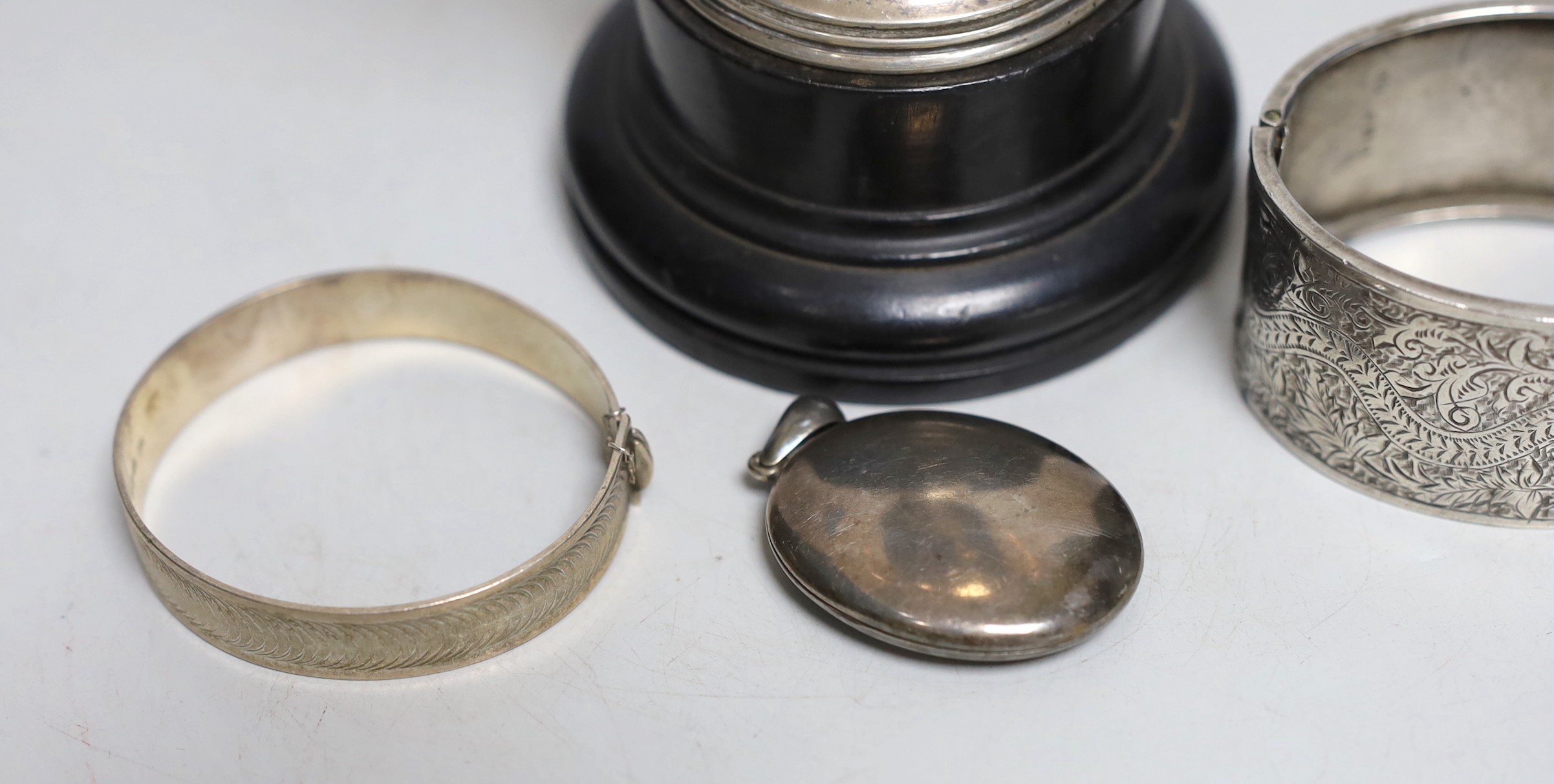 A George V silver two handled trophy cup, 19.6cm, on stand, two silver hinged bangles and a white metal locket.